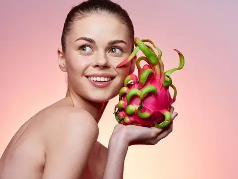 Улыбающаяся девушка с драконим фруктом на розовом фоне