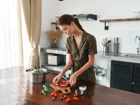 Молодая женщина режет мясо на доске на кухне