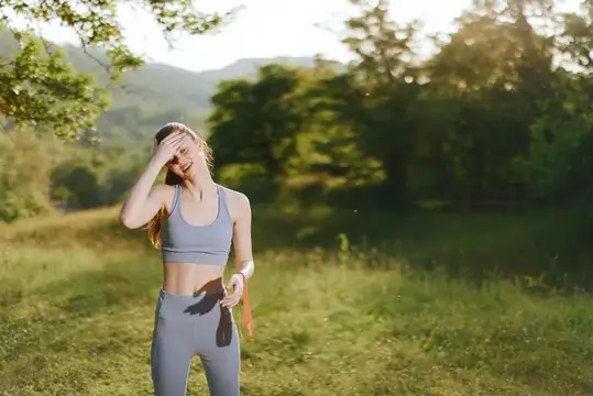 Молодая женщина в спортивной форме улыбается на фоне зелёных гор