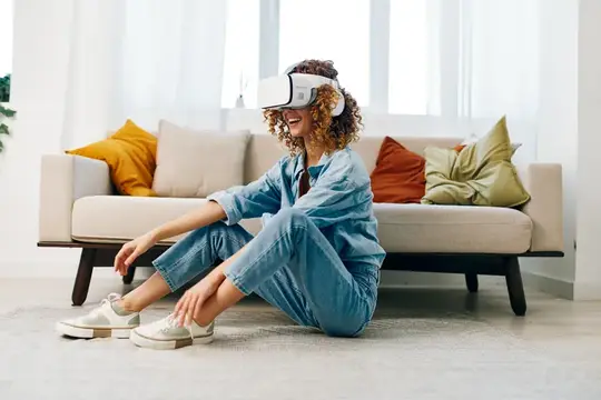 Улыбающаяся женщина наслаждается игрой в виртуальной реальности с VR-очками на диване в современной гостиной