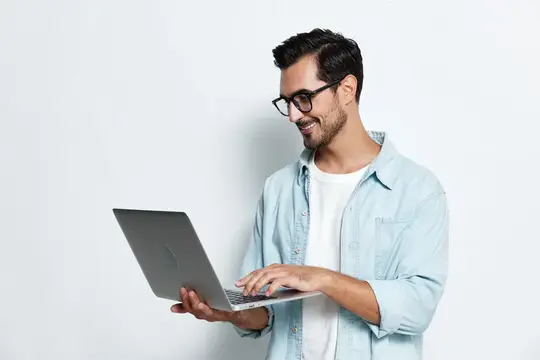 Улыбающийся бородатый мужчина в очках работает за ноутбуком на светлом фоне
