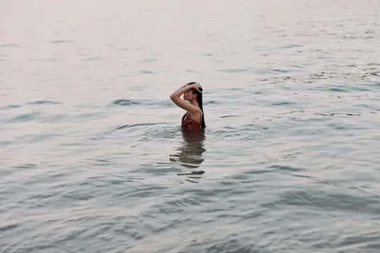 Девушка по грудь в воде придерживает волосы рукой