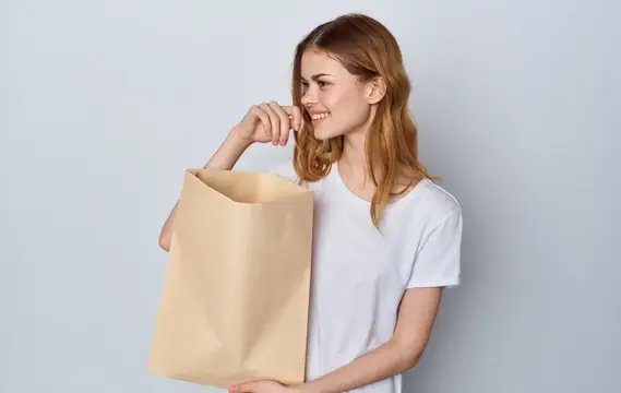 Женщина в белой футболке и джинсах с пакетом продуктов в руках