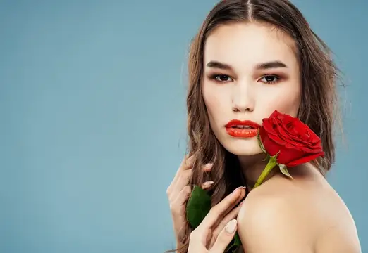 Молодая женщина с красной розой у лица на голубом фоне