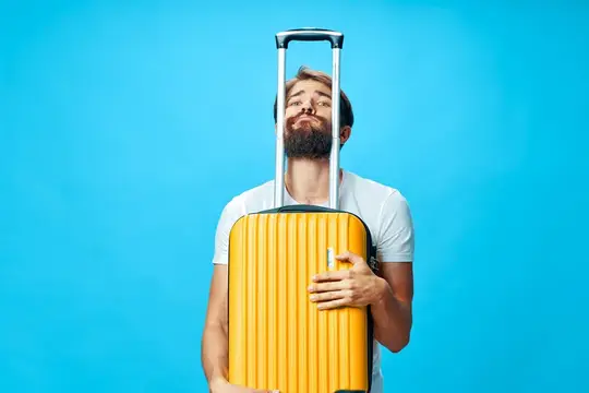Бородатый мужчина обнимает жёлтый чемодан на синем фоне