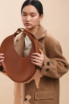 Азиатская девушка в бежевом пальто держит коричневую сумку