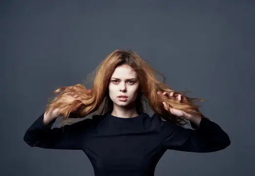 Рыжеволосая девушка растрепывает волосы на сером фоне