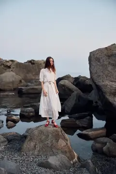 Девушка в белом платье стоит на камне у моря