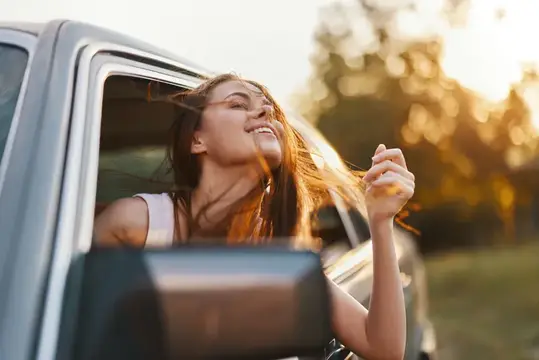 Счастливая девушка высунулась из окна машины на закате