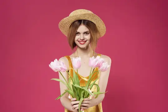 Улыбающаяся девушка в соломенной шляпе с букетом розовых тюльпанов на розовом фоне