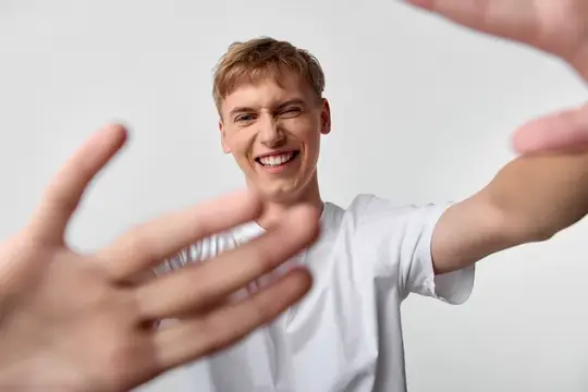 Улыбающийся парень тянет руки к камере на светлом фоне