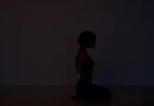 Силуэт девушки, стоящей на коленях в тёмной комнате