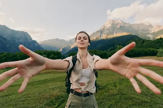 Молодая женщина с рюкзаком раскинула руки на фоне гор
