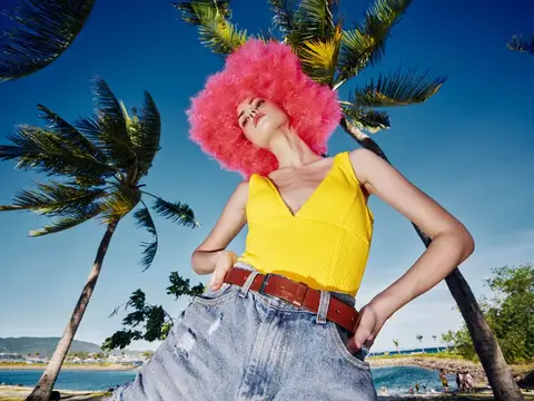 Девушка в розовом парике и жёлтом топе позирует на фоне пальм