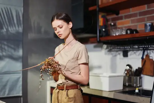 Молодая женщина с сухоцветами стоит на кухне у кирпичной стены