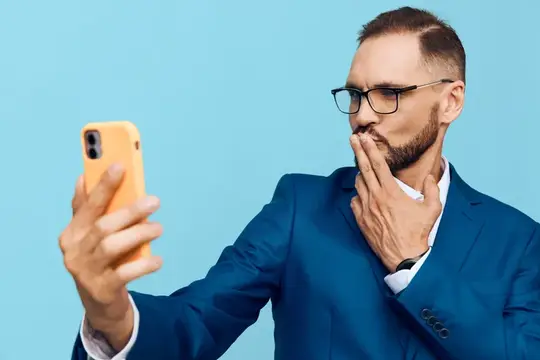 Удивлённый мужчина в очках делает селфи на жёлтый смартфон