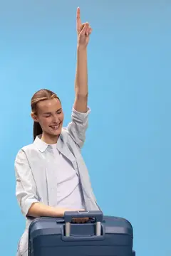 Улыбающаяся девушка с чемоданом поднимает руку вверх