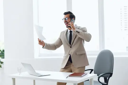 Мужчина в костюме эмоционально говорит по телефону в офисе