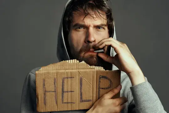 Бородатый мужчина в капюшоне с картонным плакатом Help