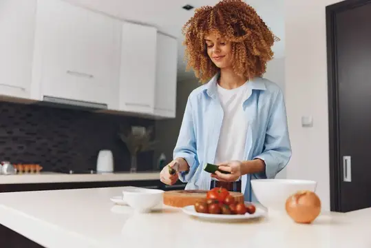 Кудрявая девушка режет овощи на светлой кухне