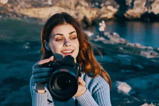 Улыбающаяся девушка с фотокамерой на фоне скалистого берега