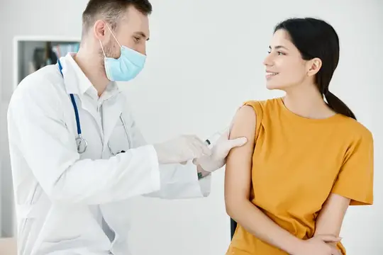 Врач в маске делает укол в плечо улыбающейся пациентке