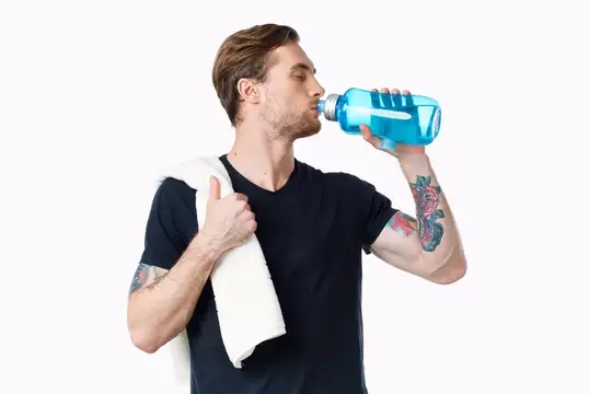 Атлетичный мужчина пьёт воду, заряжаясь энергией, с полотенцем на плече