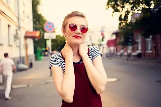Женщина в солнцезащитных очках прогуливается на открытом воздухе, передавая эмоции и позируя в модном образе
