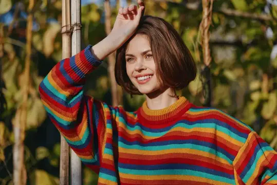 Улыбающаяся девушка в ярком полосатом свитере на фоне виноградника