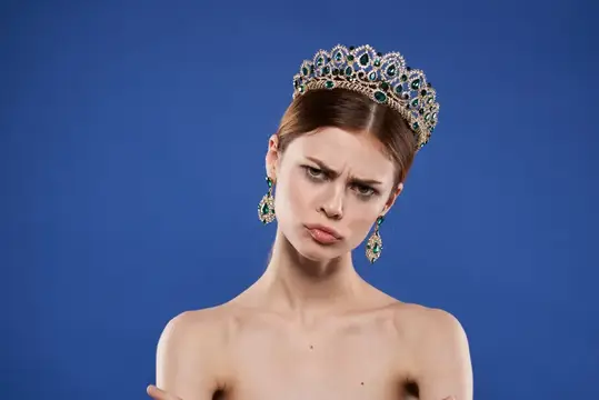 Молодая женщина в роскошной короне с недовольной гримасой на синем фоне