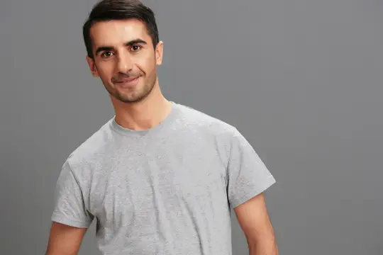 Улыбающийся темноволосый мужчина в серой футболке на сером фоне