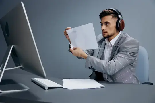 Мужчина в наушниках изучает документ перед монитором в офисе