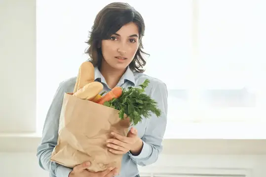 Молодая женщина с бумажным пакетом продуктов у окна