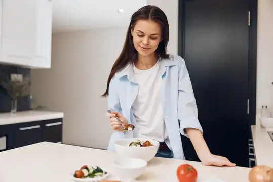 Молодая женщина готовит салат на светлой кухне