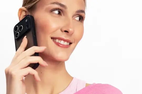 Молодая женщина с чистой кожей пользуется смартфоном, улыбаясь и отводя взгляд в сторону на белом фоне