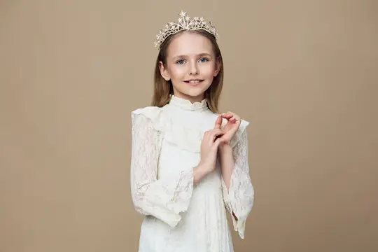Улыбчивая девочка в белом платье и короне на бежевом фоне