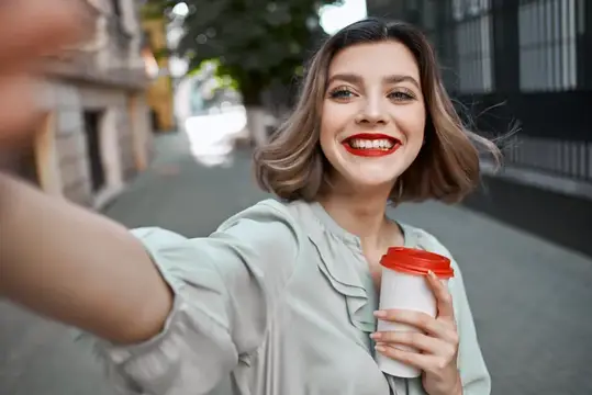 Жизнерадостная женщина делает селфи на улице с чашкой кофе