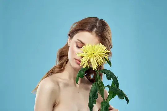 Красивая женщина с жёлтым цветком у лица, улыбающаяся, кадрированный портрет с обнажёнными плечами