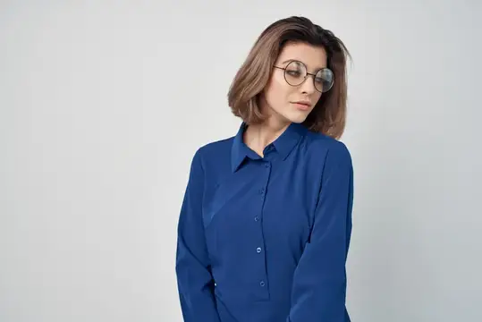 Молодая женщина в очках и синей рубашке смотрит в сторону