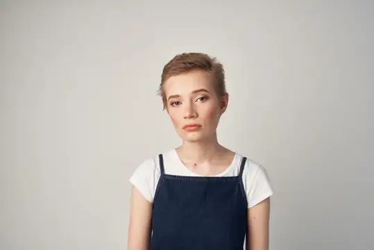 Молодая женщина с короткой стрижкой в тёмном сарафане на сером фоне