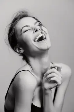 Молодая женщина искренне смеётся, запрокинув голову, на светлом фоне
