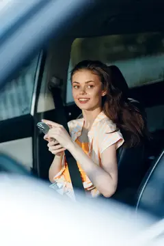 Улыбающаяся темноволосая девушка с телефоном на заднем сиденье автомобиля