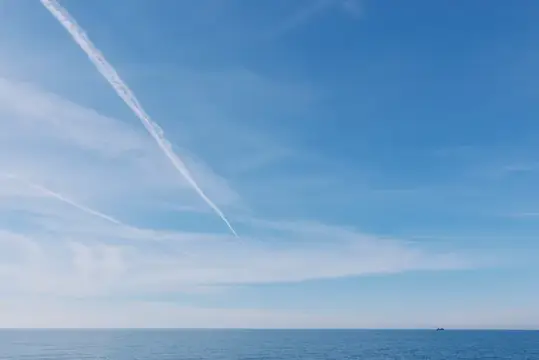 Безмятежный морской пейзаж: спокойная вода, бесконечный горизонт и одинокий инверсионный след под ярким голубым небом
