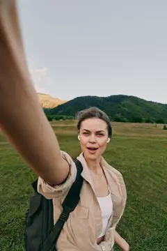 Улыбающаяся девушка с наушниками делает селфи на фоне гор