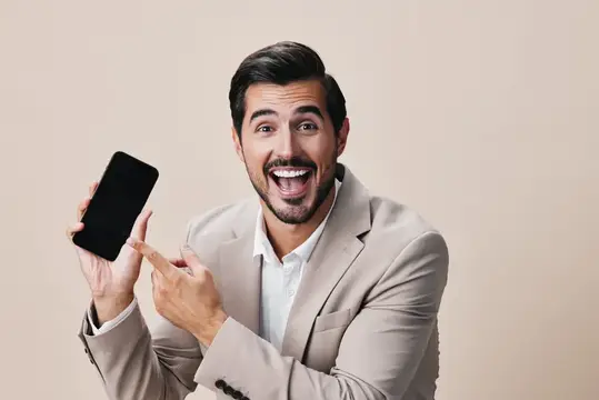 Удивлённый мужчина в бежевом пиджаке показывает на смартфон