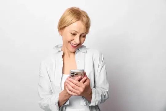 Женщина со смартфоном улыбается, пожилая, коммуникация, технологии, помещение, белый фон, портрет крупным планом