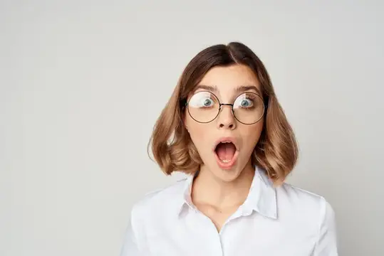 Удивлённая девушка в очках с открытым ртом на сером фоне