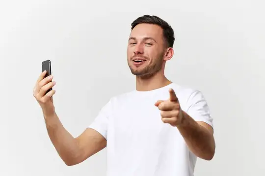 Улыбающийся мужчина с телефоном указывает пальцем на зрителя