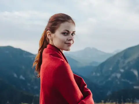 Женщина-путешественница с красным пледом на плечах в горах