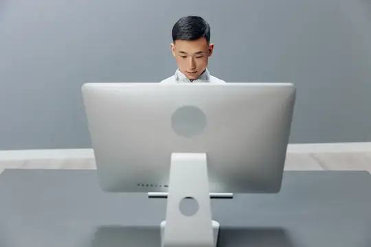 Азиатский мужчина работает за белым компьютером на сером фоне